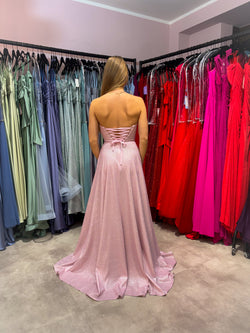 Glitzerndes Abiballkleid in zartem Rosa mit trägerlosem Bustieroberteil und Rock in A-Linie. Das Kleid hat eine Rückenschnürung und einen hohen Beinschlitz sowie seitliche Einschubtaschen.